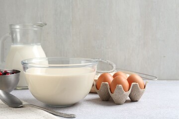 Liquid dough in bowl, berries and ingredients on light grey table, closeup