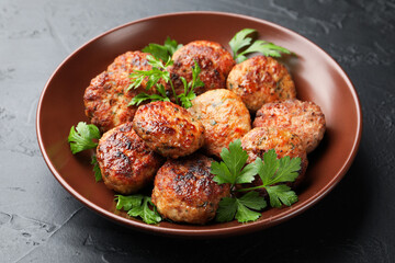 Delicious patties with parsley in bowl on dark textured table, closeup