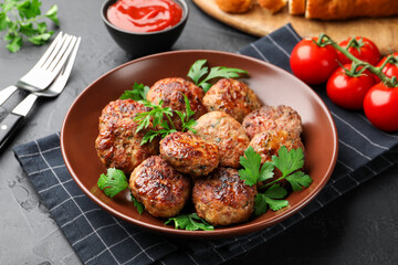 Delicious patties with parsley in bowl on dark textured table, closeup