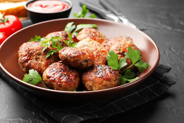 Delicious patties with parsley in bowl on dark textured table, closeup