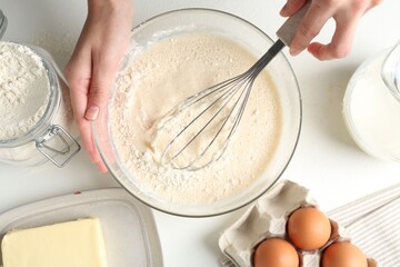 Woman making batter (liquid dough) at white table, top view