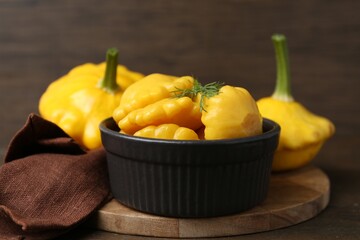 Pickled pattypan squashes in bowl and fresh vegetables on wooden table, closeup