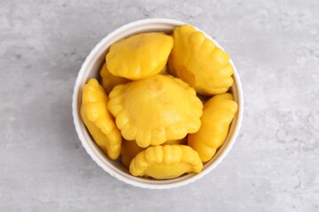 Pickled pattypan squashes in bowl on light grey table, top view