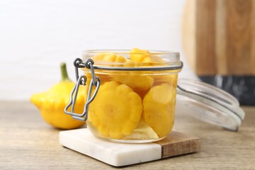 Pickled pattypan squashes in glass jar on wooden table, closeup