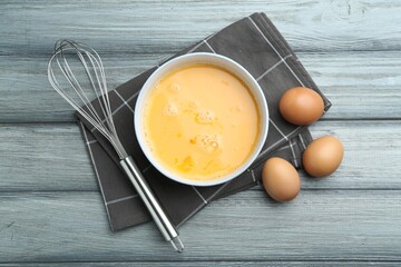 Beaten eggs in bowl and whisk on wooden table, flat lay