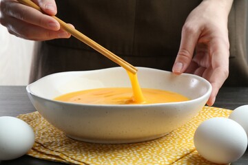 Woman whisking eggs in bowl at table, closeup