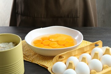 Raw eggs, yolks in bowl and flour on table, closeup
