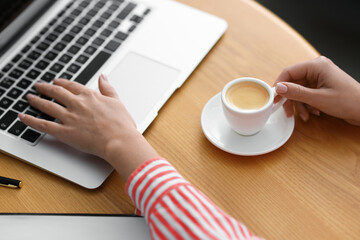 Coffee break. Woman with laptop and cup at wooden table, closeup