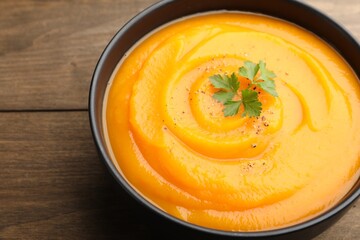 Tasty pumpkin cream soup with spices in bowl on wooden table, closeup