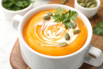 Tasty pumpkin cream soup with parsley and seeds in bowl on table, closeup