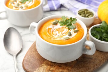 Tasty pumpkin cream soup with parsley and seeds served on light table, closeup