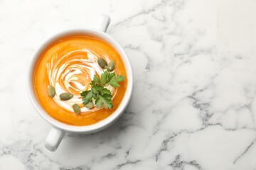 Tasty pumpkin cream soup with parsley and seeds in bowl on white marble table, top view. Space for text