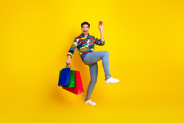 Obraz premium Young man in colorful shirt jumps with shopping bags and takes a selfie against a bright yellow background expressing joy and fun shopping fashion and leisure