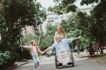 Joyful family outing in the park as grandpa in wheelchair shares a smile with granddaughter and...