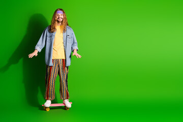 Cheerful man with long hair on the green background posing with skateboard wearing a colorful vintage-inspired outfit.
