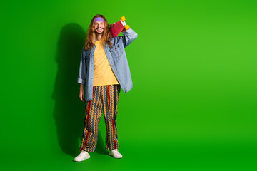 Casual young man with long hair holding skateboard on green background exuding hippie retro style and cheerful energy