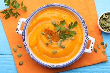 Delicious pumpkin cream soup with parsley and seeds served on blue wooden table, flat lay