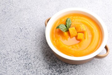 Delicious pumpkin cream soup with basil served on grey table, closeup. Space for text
