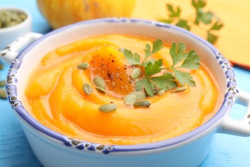 Delicious pumpkin cream soup with parsley and seeds served on blue wooden table, closeup