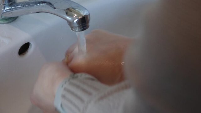 Close-up sequence of hands under running water from a faucet, showcasing the washing process with gradual camera zoom, highlighting water flow and hand movements in a clean, bright environment