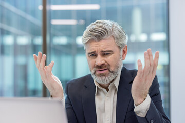Experienced businessman showing confusion and exasperation while working on a laptop. Indicating challenges with technology. A technical issue. Or feeling stressed and burnt out in a corporate setting
