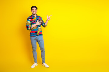 Fototapeta premium Young man in colorful shirt poses against bright yellow background smiling and pointing