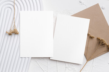 Blank stationery mock up with two white cards and brown envelope on textured background, featuring dried flowers, ideal for wedding invitations designs
