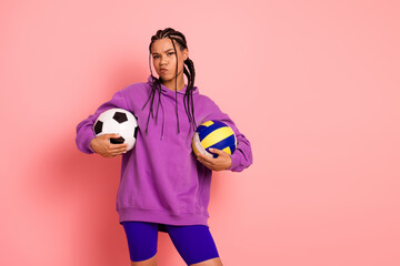 Young woman in sportswear holding soccer and volleyball balls, posing confidently against a vibrant pink background
