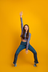 Energetic young woman with raised arm in bright checkered crop top and jeans dancing against a...