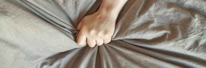 Caucasian female hand gripping wrinkled gray fabric with tightly closed fist, expressing strong...