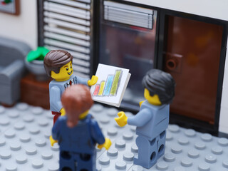 Obraz premium Tambov, Russian Federation - October 23, 2025 Happy Lego businesspeople minifigures having a meeting and discussing graphs showing the results of their successful teamwork.