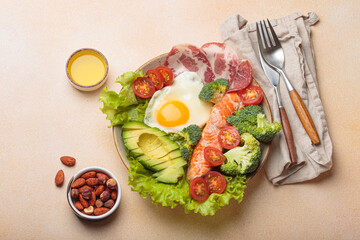 Healthy ketogenic diet concept showing a balanced meal on plate with salmon, avocado, fried egg, bacon, broccoli, tomato, and fresh salad, promoting low carb and high fat eating