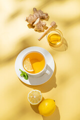 Hot tea with lemon, ginger, honey, and mint in a cup on a bright yellow background with citrus fruits