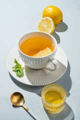 Hot tea with lemon, honey, and mint in a cup on a blue background with citrus fruits, spoon and shadows.