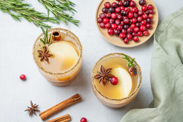 Two glasses of apple cider with cinnamon, anise, brown sugar and rosemary on a light background