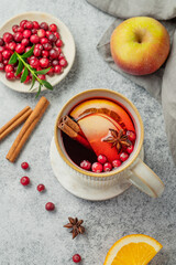 A hot cranberry Christmas drink in a mug on a gray background with cinnamon, berries and fruits.