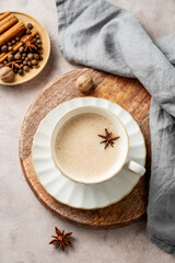 Traditional Indian masala chai tea with milk and spices in a white cup on a wooden board on a light background