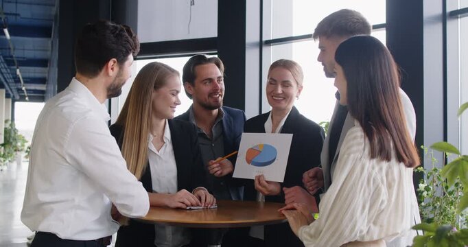 Business team is engaged in productive discussion about graphs and data analysis. Colleagues gather around round table in modern office environment and discuss strategic planning. 4k video footage.