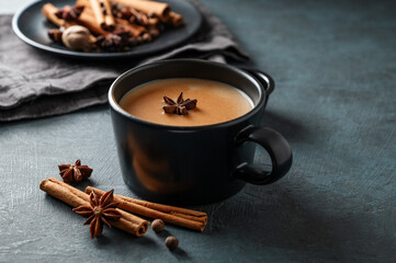Traditional Indian masala chai tea with milk and spices in a black cup on a dark background close up.