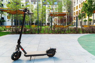 Modern electric scooter parked on a paved area in the landscaped courtyard of a residential complex with hammocks and apartment buildings in the background