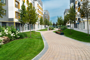 A curving paved path through the green lawn and young trees of a well-landscaped courtyard in a modern residential apartment block complex