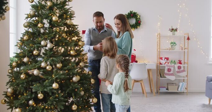 Family happy decorating Christmas tree at home New Year holiday parents and small kids, xmas balls decor seasonal preparation, enjoying traditional winter holidays together near beautiful Xmas firtree