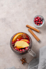 A cup of red mulled wine with spices, orange, apple slices and cranberry on a light background
