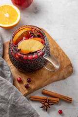A cup of red mulled wine with spices, orange and apple slices on a wooden board on a light background