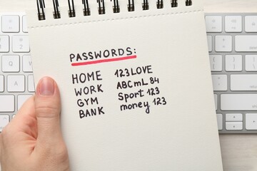 Woman holding notebook different passwords at table, top view