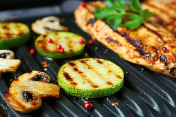 Tasty mushrooms, spices, zucchini and chicken fillet on black electric grill, closeup