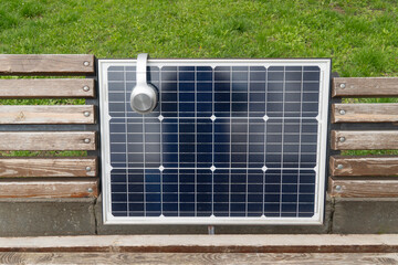Headphone resting on a dark blue solar panel integrated into a wooden bench, symbolizing renewable energy and outdoor public charging technology