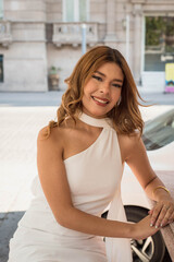 Elegant young woman in chic white dress posing confidently at a stylish outdoor cafe seating area on a sunny day