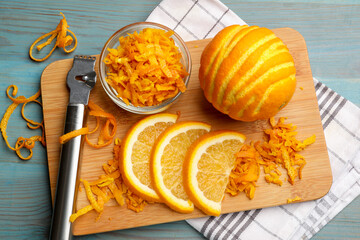 Orange zest, fresh fruits and zester tool on light blue wooden table, flat lay