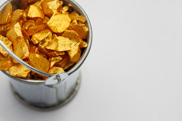 Small metal bucket filled with golden stones on white background. Concept of wealth